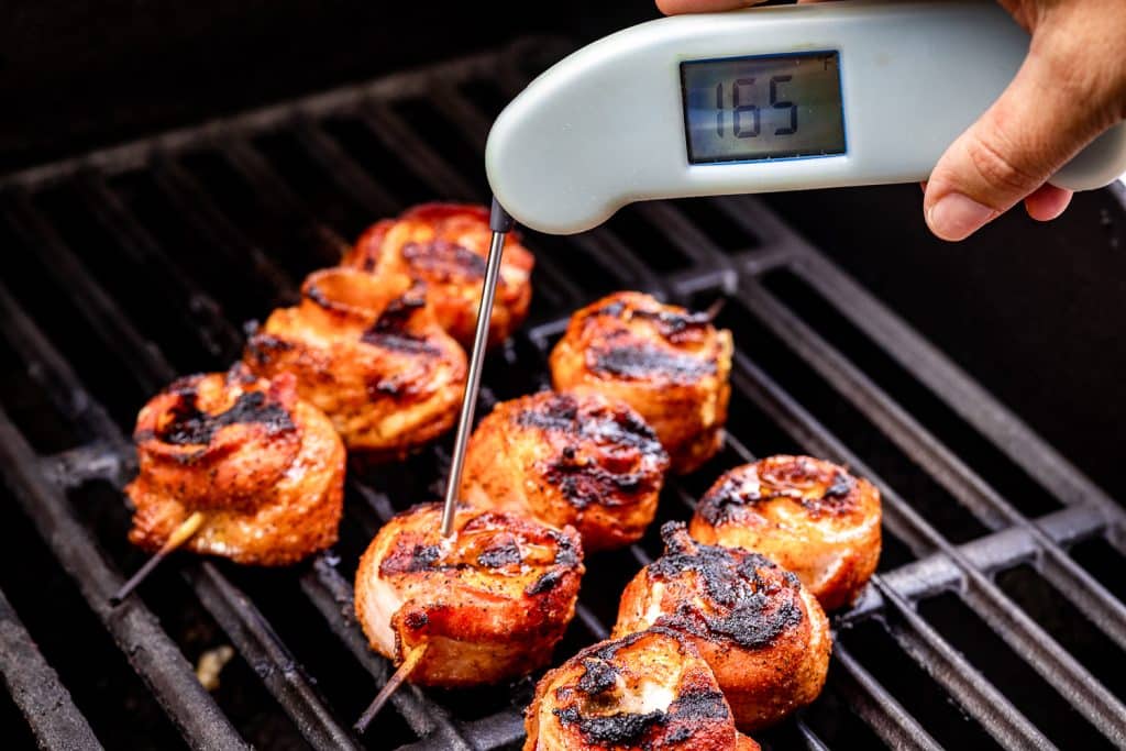 Chicken bacon lollipops on the grill with an instant read thermometer reading 165 degrees F.