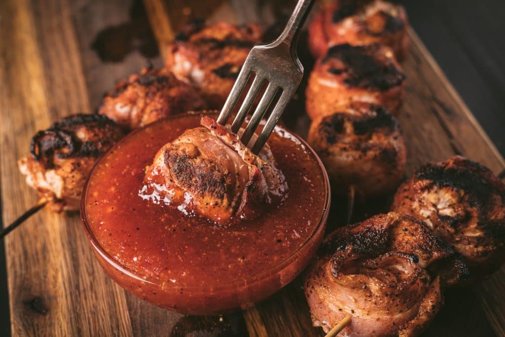 Chicken bacon lollipop on a fork being dipped into sauce.