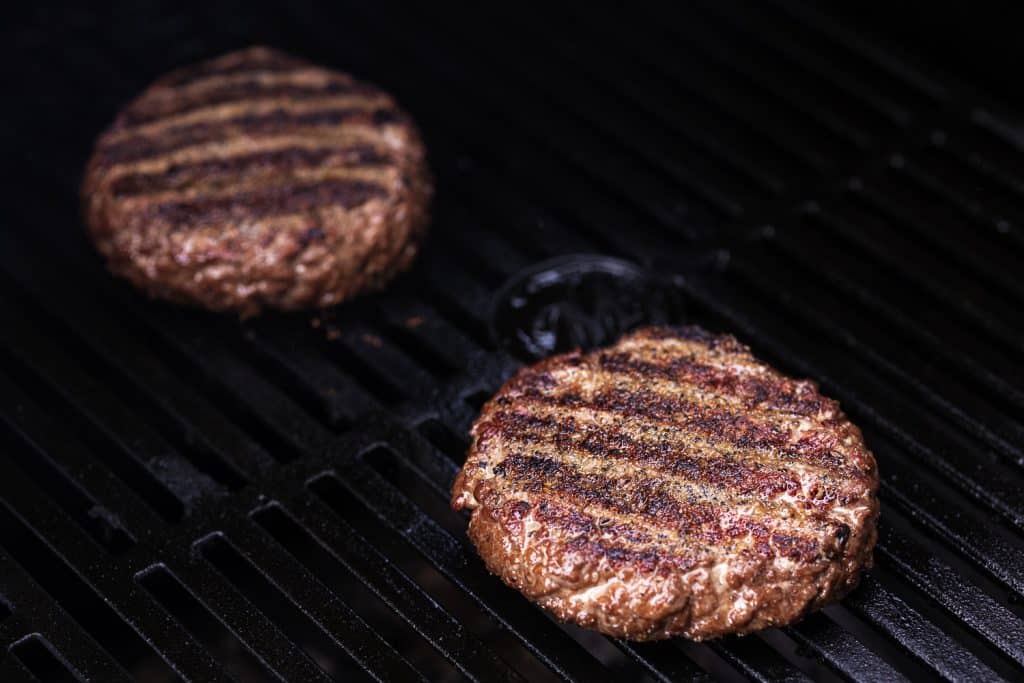 Two grass-fed beef burger patties on the grill.