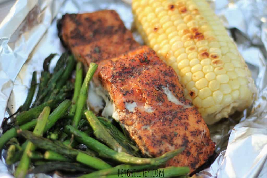Close up of grilled asparagus, seasoned and grilled salmon, and a half ear of grilled corn in a aluminum foil packet.