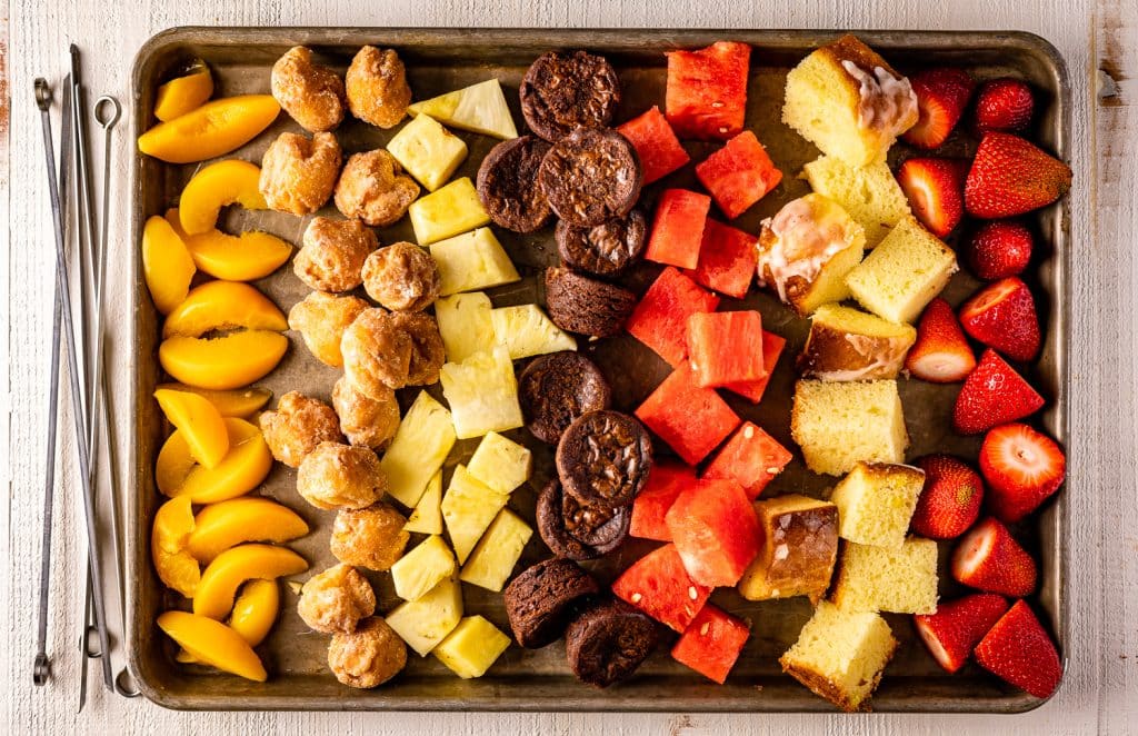 Ingredients for dessert and fruit kabobs on a baking dish.