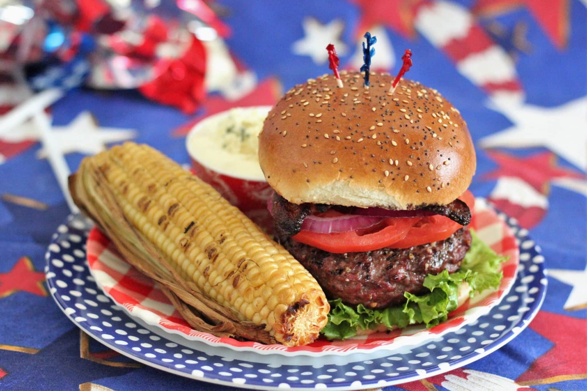 assembled stuffed burger on a red plate with whole grilled corn.