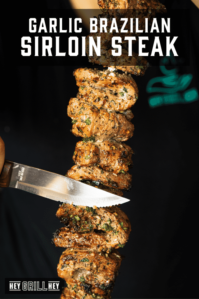 Knife slicing through marinated garlic Brazilian steaks on a skewer with text overlay - Garlic Brazilian Sirloin Steak.
