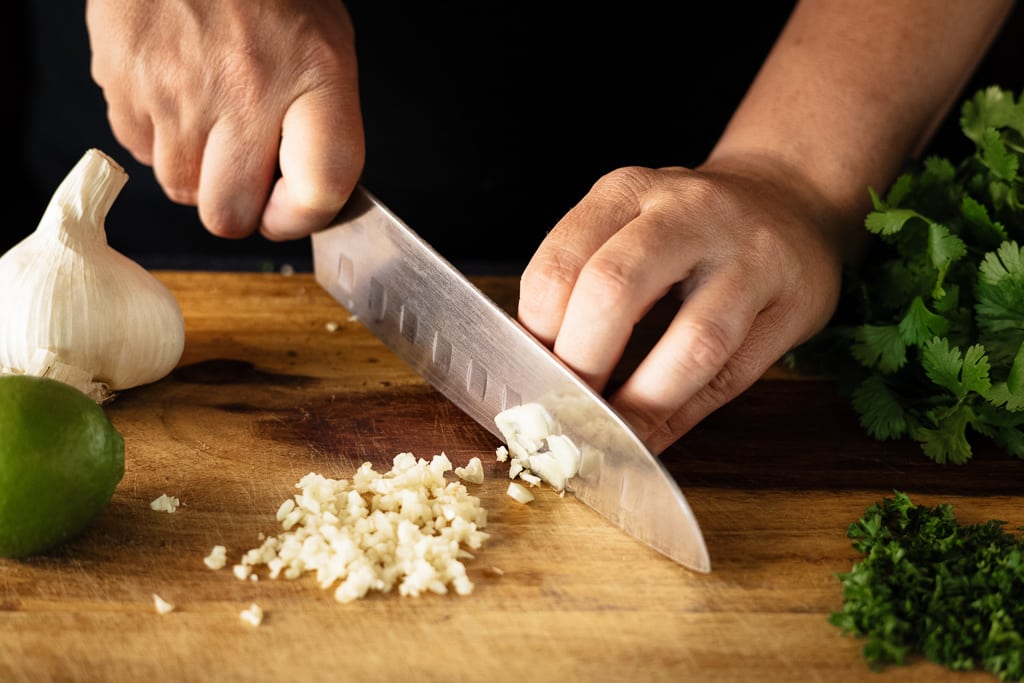 Chef dicing garlic on a large wooden cutting board.