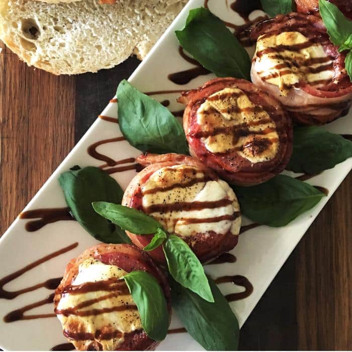bacon wrapped stuffed grilled tomatoes on a white serving platter