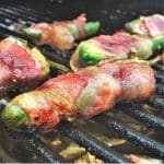 Four raspberry cream cheese jalapeno poppers on the grill grates of a pellet smoker.