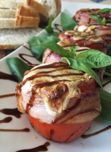 Close up view of Bacon wrapped grilled tomatoes served on a white platter and drizzled with balsamic vinegar