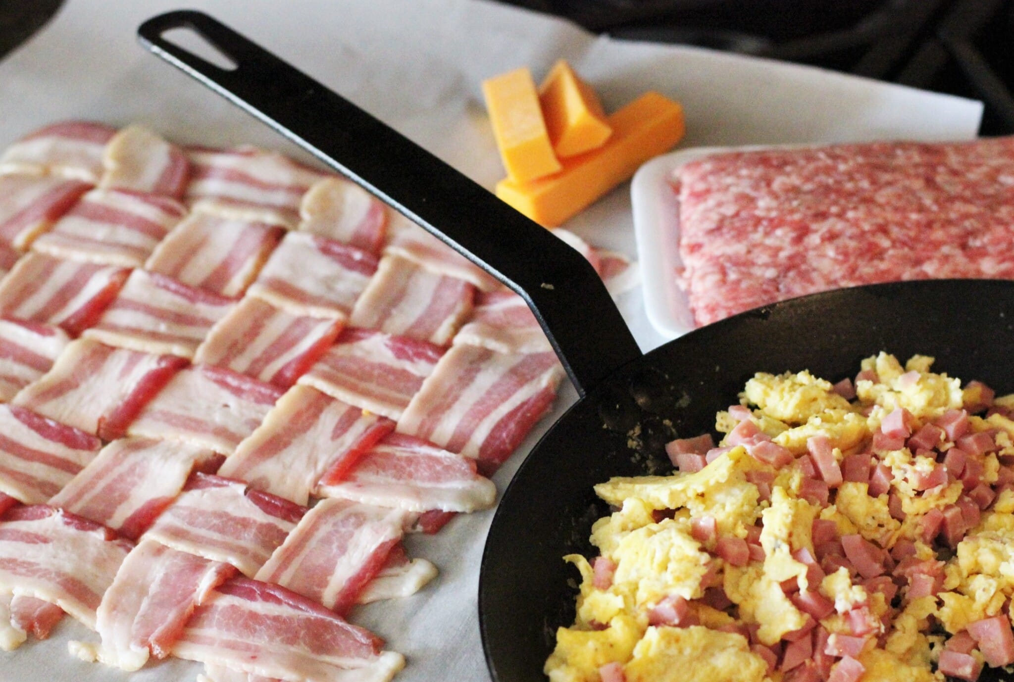 pan of eggs and ham next to a bacon weave on wax paper.