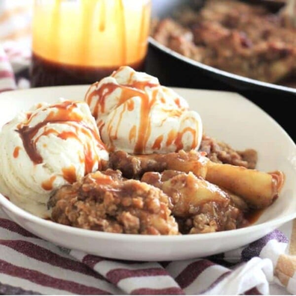 Skillet bacon apple crisp topped with two scoops of vanilla ice cream and drizzled with caramel in a white bowl.