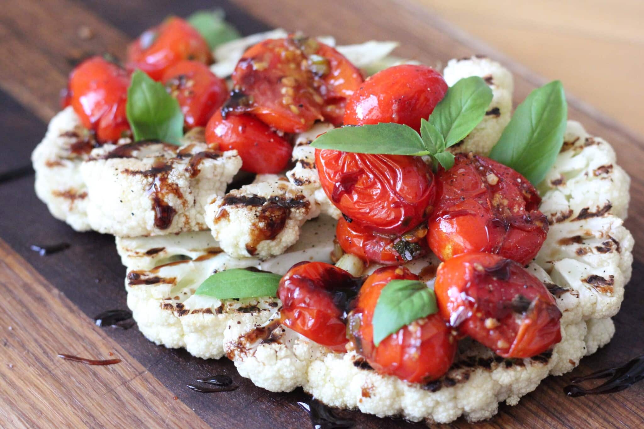 grilled cauliflower steaks with burst tomato salad on a wooden cutting board.