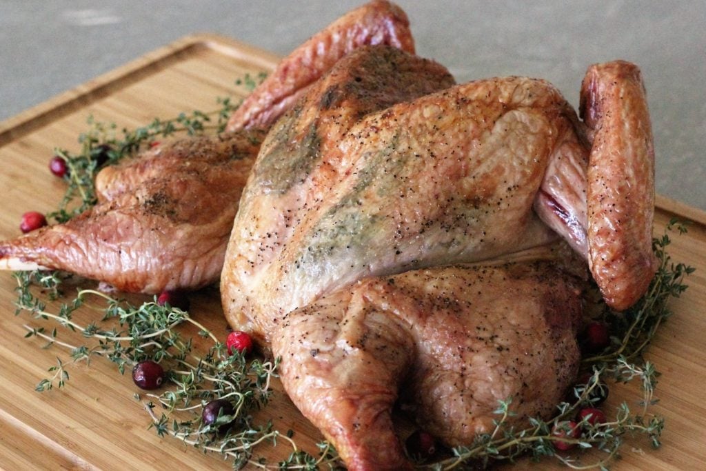 whole smoked spatchcock turkey on a wooden cutting board with herbs and cranberries