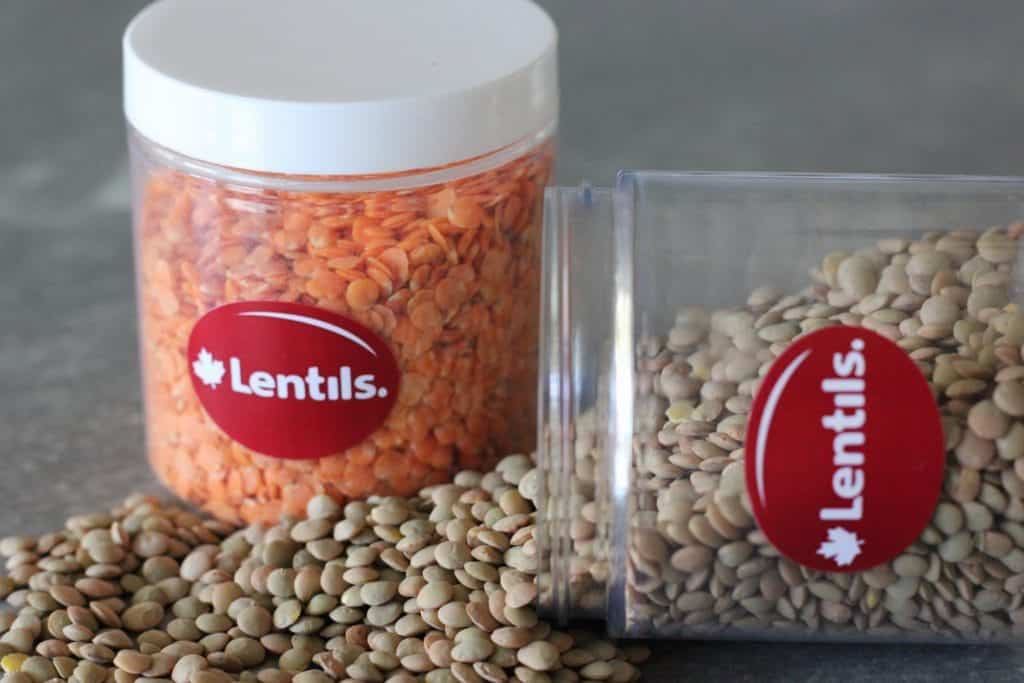 Two glass jars. One with red lentils, one with green lentils. The green lentils are tipped over and are spilling out.