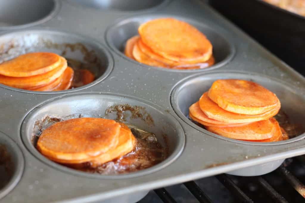 Sweet potato slices stacked in a muffin tin in a melted butter and brown sugar sauce.