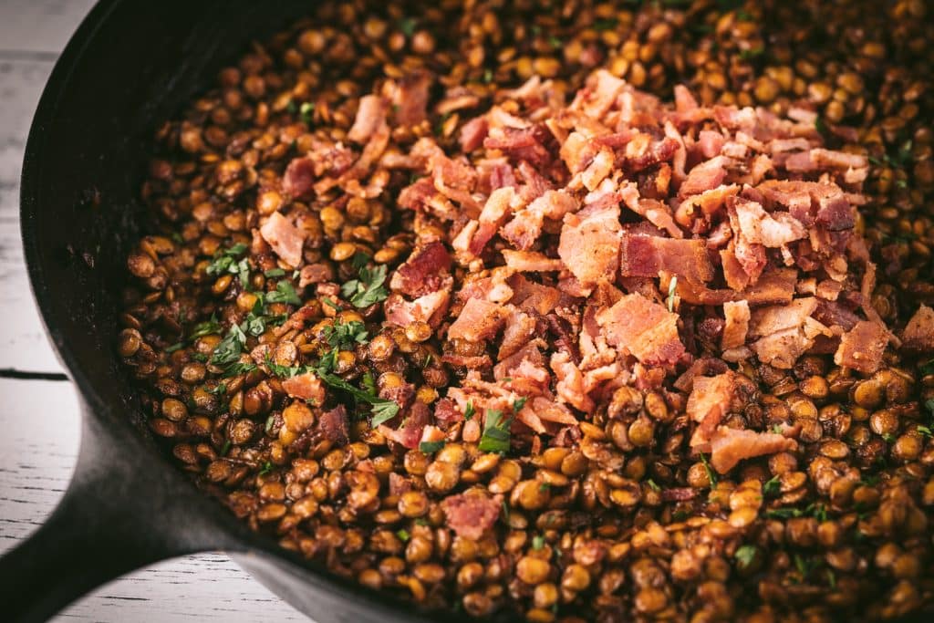 BBQ baked lentils in a cast iron skillet topped with bacon.
