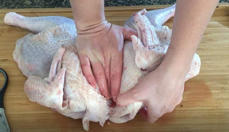 hand pressing down on a turkey to flatten it on a wooden cutting board