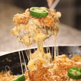 A spoonful of cheesy jalapeno popper mac and cheese being lifted out of a cast iron skillet.