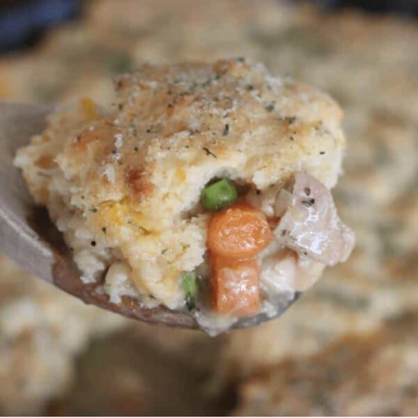 Close up of chicken pot pie with cheddar biscuit crust on a wooden spoon.