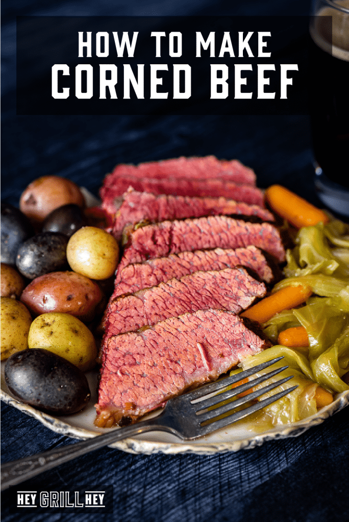 Sliced corned beef on a plate with whole roasted potatoes, cabbage and baby carrots. Text overlay reads: How to Make Corned Beef.