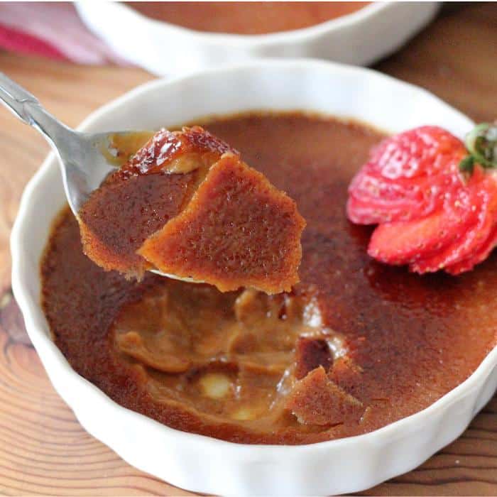 Metal spoon taking a scoop out of a white bowl of caramel creme brulee.