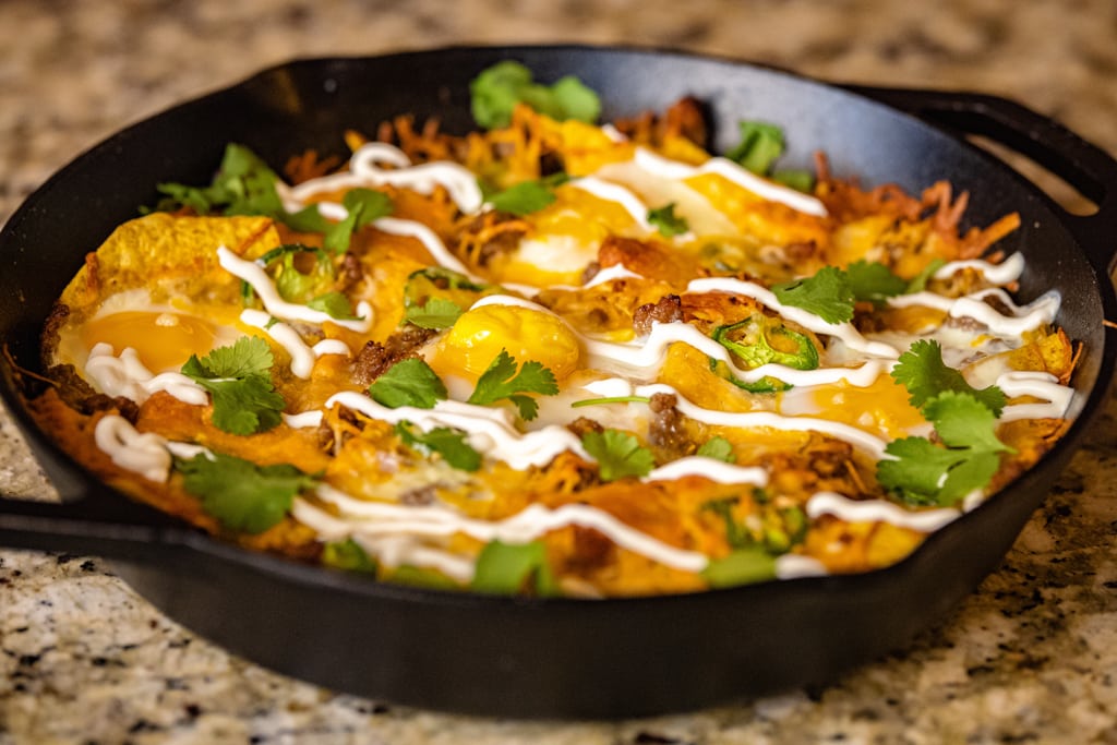 Breakfast nachos in a cast iron skillet topped with sour cream and fresh cilantro.