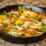Loaded breakfast nachos in a cast iron skillet garnished with sour cream and fresh cilantro.