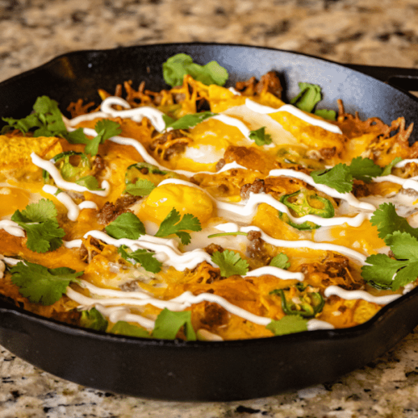 Loaded breakfast nachos in a cast iron skillet garnished with sour cream and fresh cilantro.