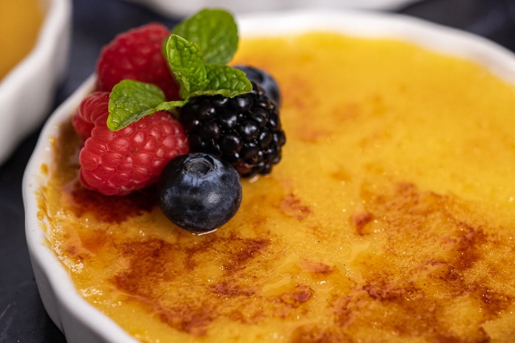 One ramekin of caramel creme brulee topped with fresh berries and a mint leaf.