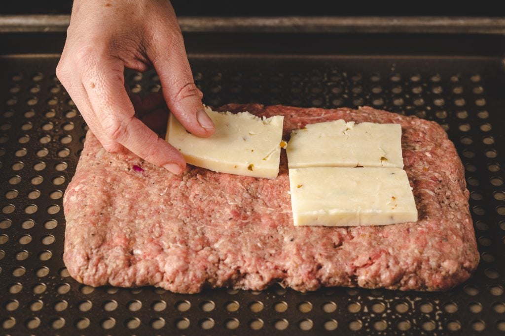 Pepperjack cheese being added to a layer of meatloaf.