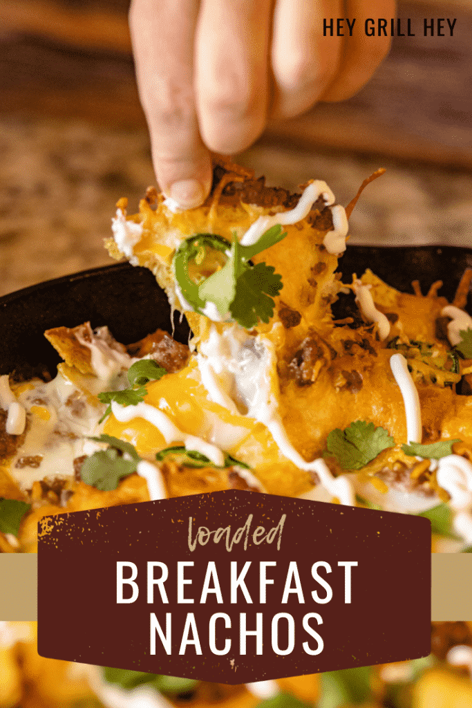 Loaded breakfast nacho being pulled out of a skillet full of breakfast nachos. Text overlay reads: Loaded Breakfast Nachos.