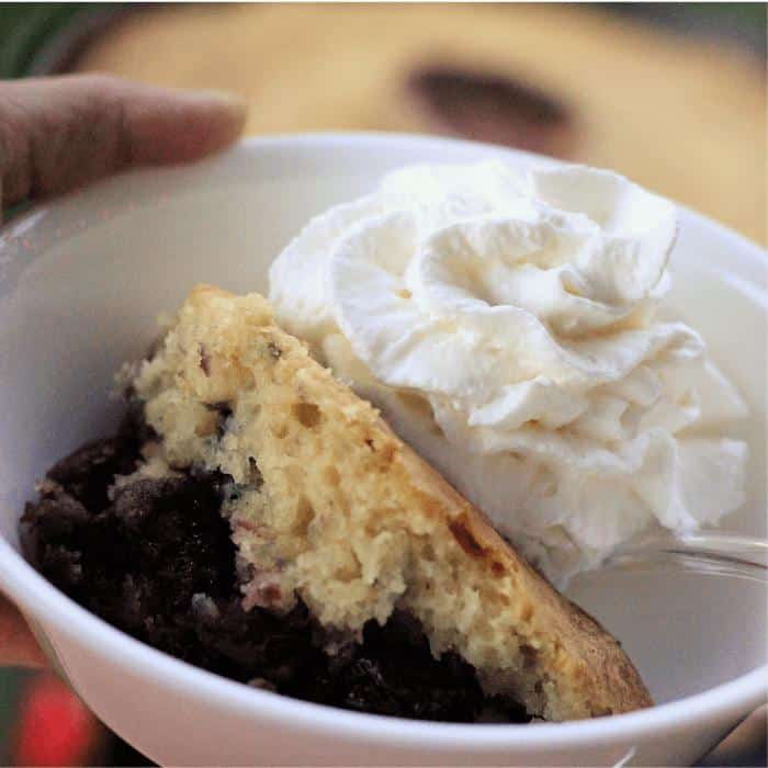 Cherry berry dutch oven cobbler and whipped cream in a white bowl.