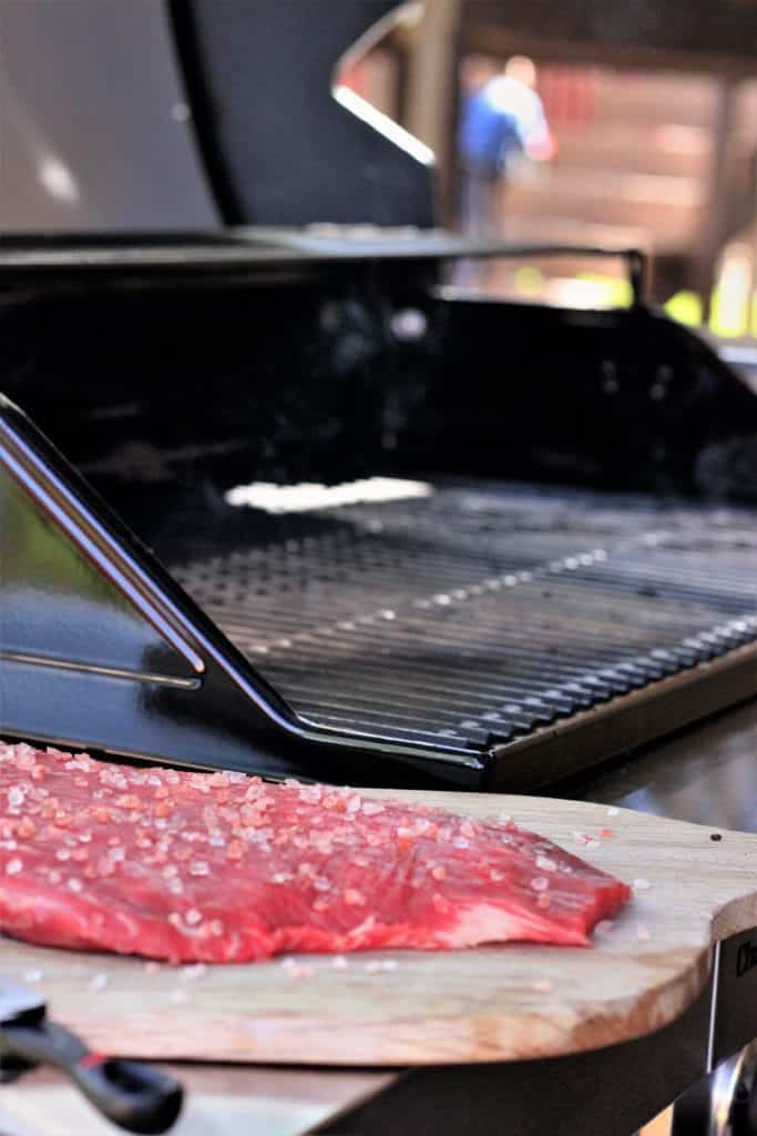 himalayan salted flank steak on a wooden cutting board next to a gas grill