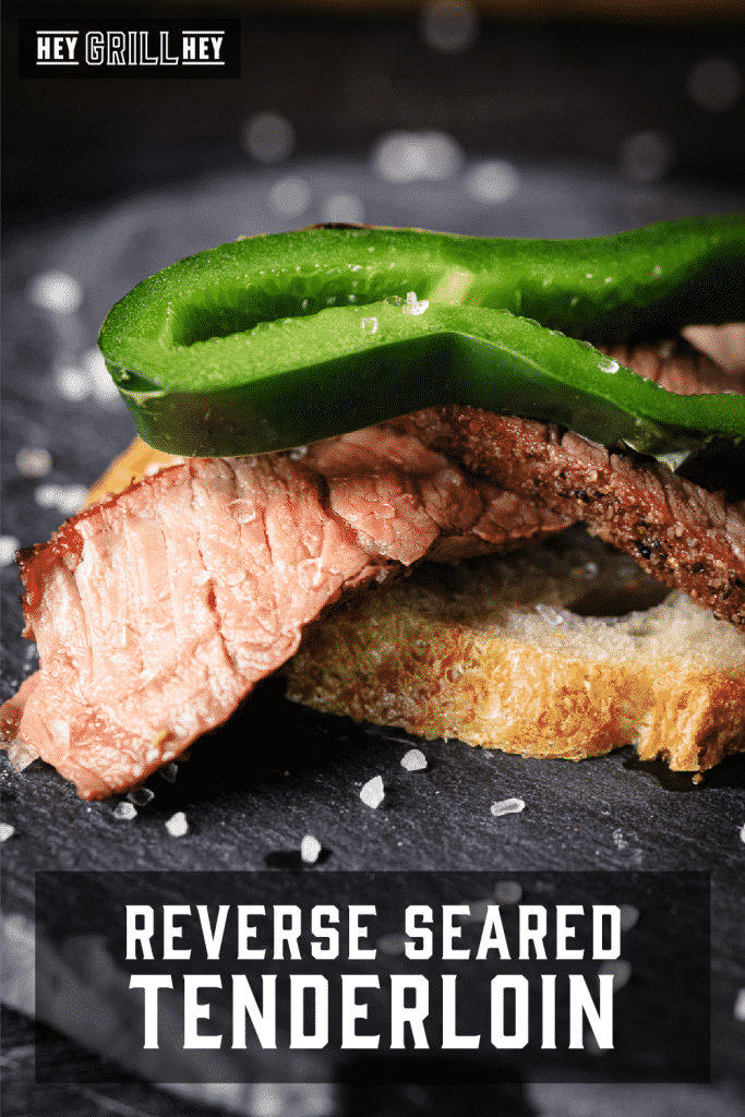 Sliced reversed seared tenderloin topped with a slice of anaheim chile on a roasted crostini with text overlay - Reverse Seared Tenderloin.