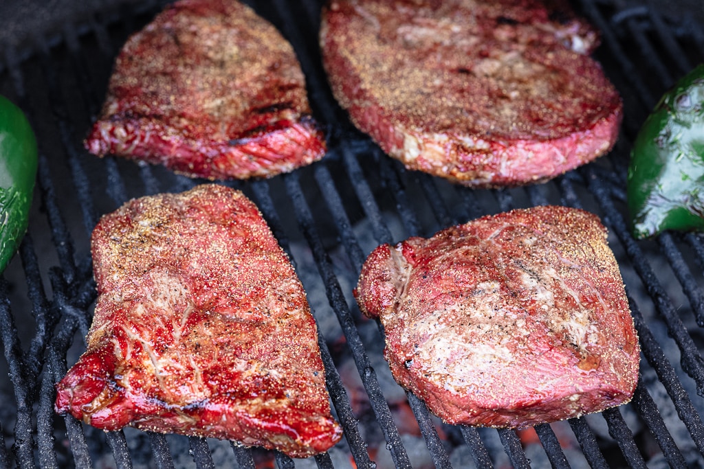 Seasoned steaks on the grill grates of a smoker.