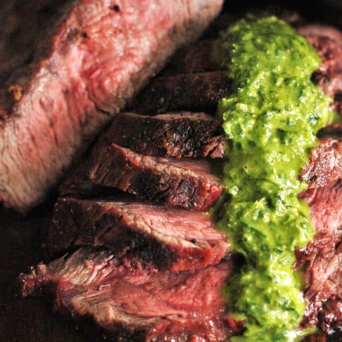 sliced grilled flat iron steak with chimichurri drizzled on the top