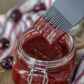 Cherry chipotle bbq sauce in a glass jar with a basting brush dipping into the sauce.