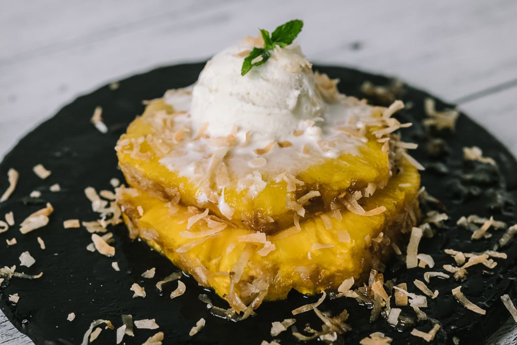 Two rings of pina colada grilled pineapple topped with a scoop of ice cream.