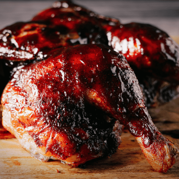 Spatchcock smoked chicken covered with cherry chipotle BBQ sauce on a wooden cutting board.