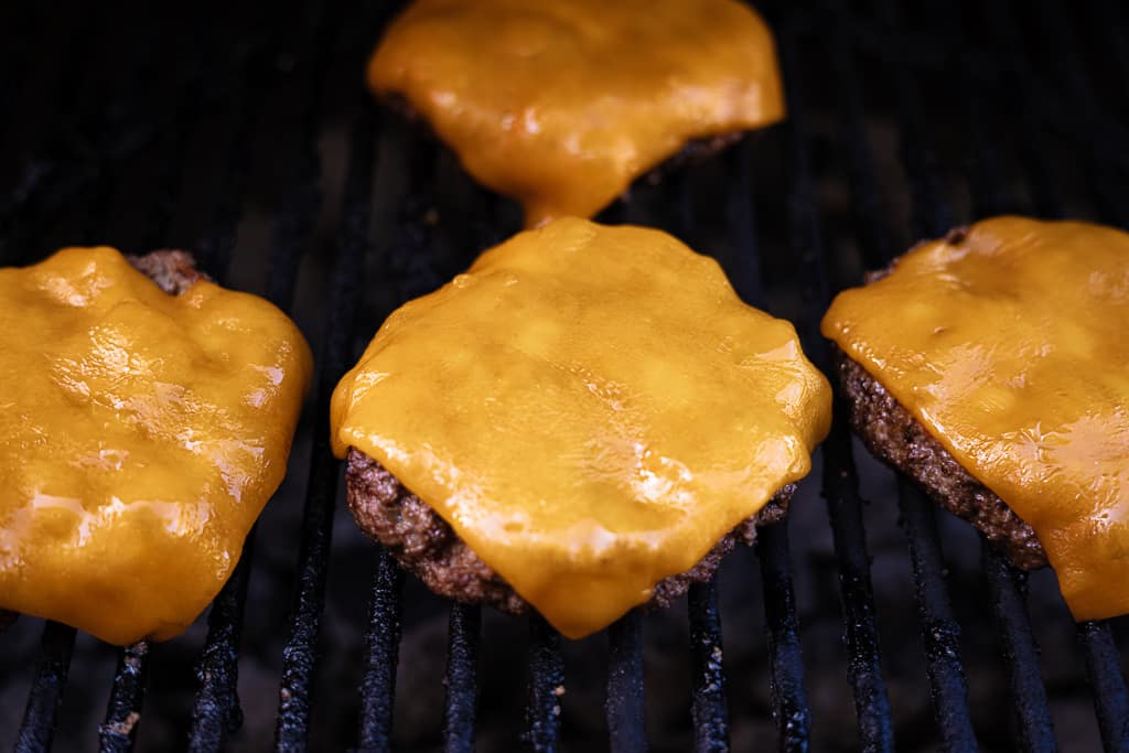 Butter burger patties topped with cheddar cheese on the grill.