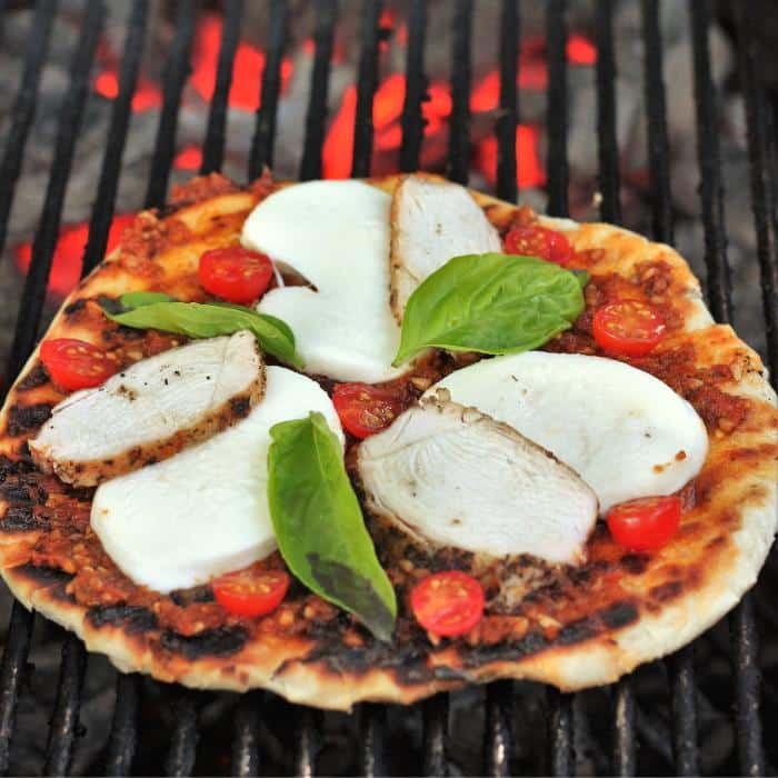 wood fired pizza with red pesto and grilled chicken on a grill over hot coals