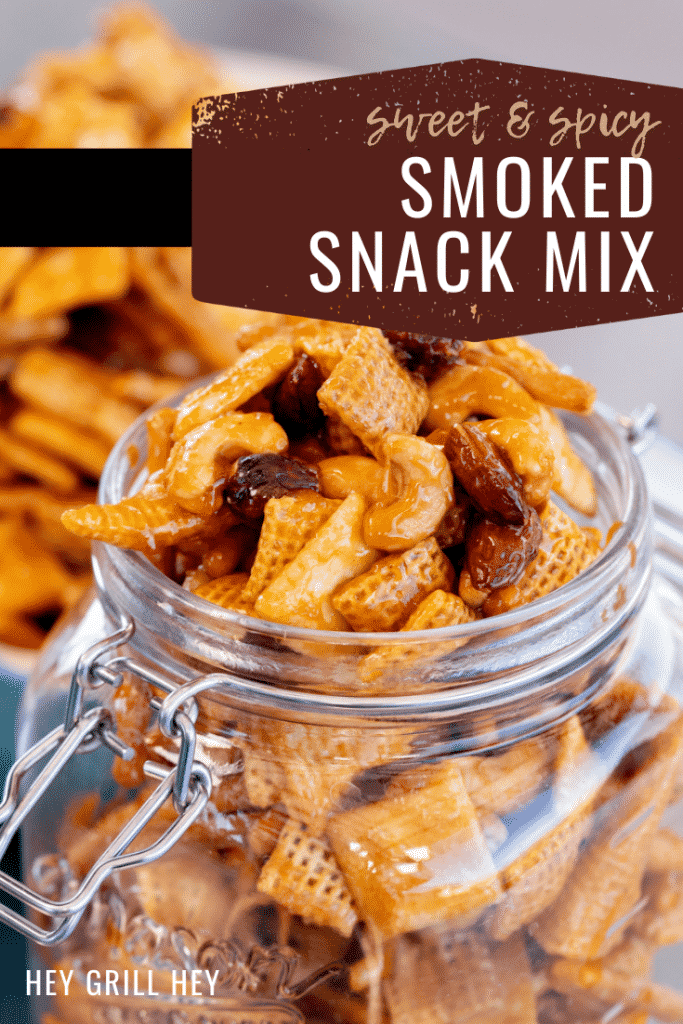 Smoked snack mix in a hinged glass mason jar with a baking dish of snack mix in the background. Text overlay reads: Sweet & Spicy Smoked Snack Mix.
