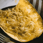 Grilled spaghetti squash on a serving dish next to a metal fork.
