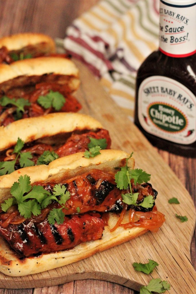 Honey Chipotle Country Style Rib Sandwich topped with cilantro on a wood cutting board with a bottle of barbecue sauce in the background.