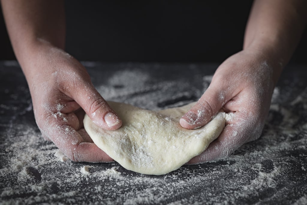 Pizza dough being shaped on a floured surface.
