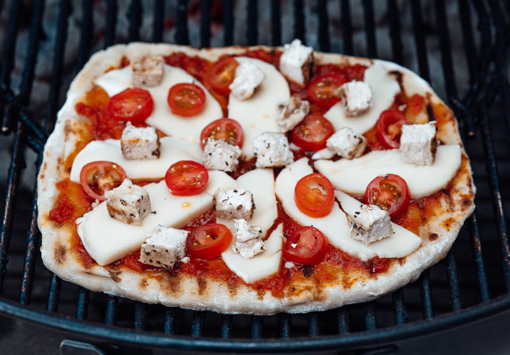 Homemade pizza being cooked on a charcoal grill.