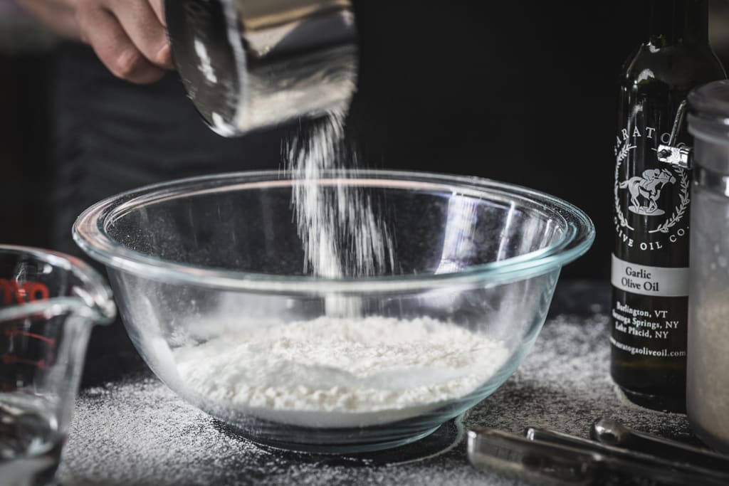 Flour being sprinkled into a large glass bowl.