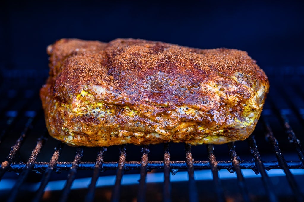 Seasoned pork butt on the grill grates of a pellet smoker.