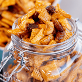 Smoked snack mix in a hinged glass mason jar with a baking dish of snack mix in the background.