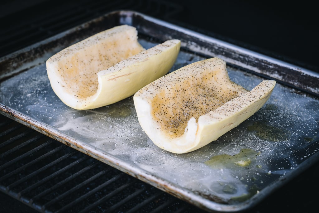 Two seasoned spaghetti squash halves on a baking dish in a grill.