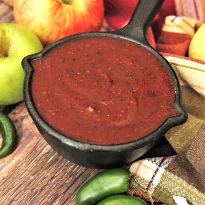 Apple jalapeno BBQ sauce in a metal bowl surrounded by whole fresh apples and jalapenos.