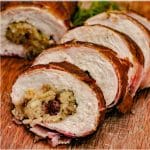 Bacon wrapped turkey breast roulade sliced and lined up on a wooden cutting board.